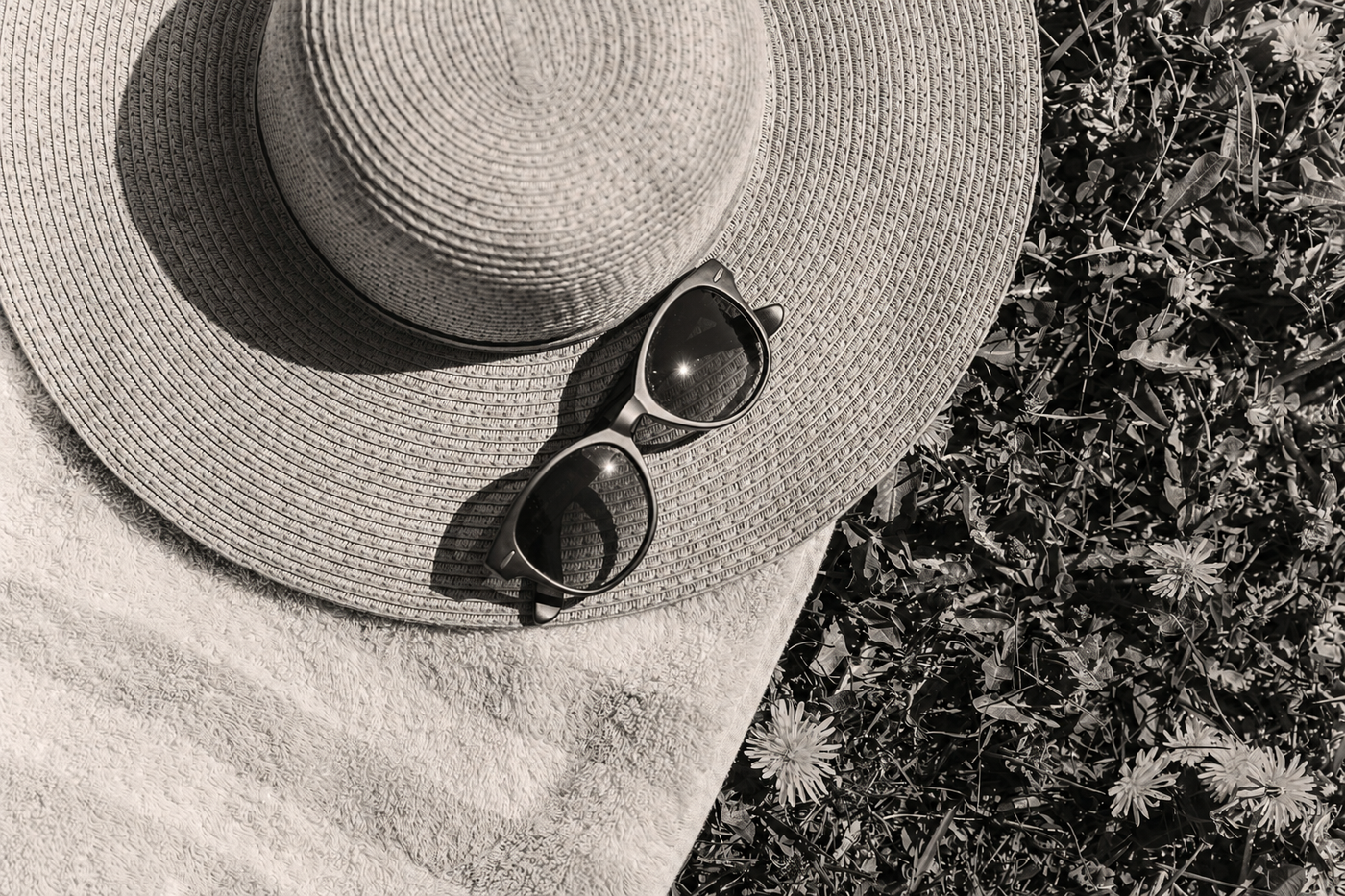 A faceless wooden figure wearing a wide-brimmed summer hat in a garden, in soft warm black and white.
