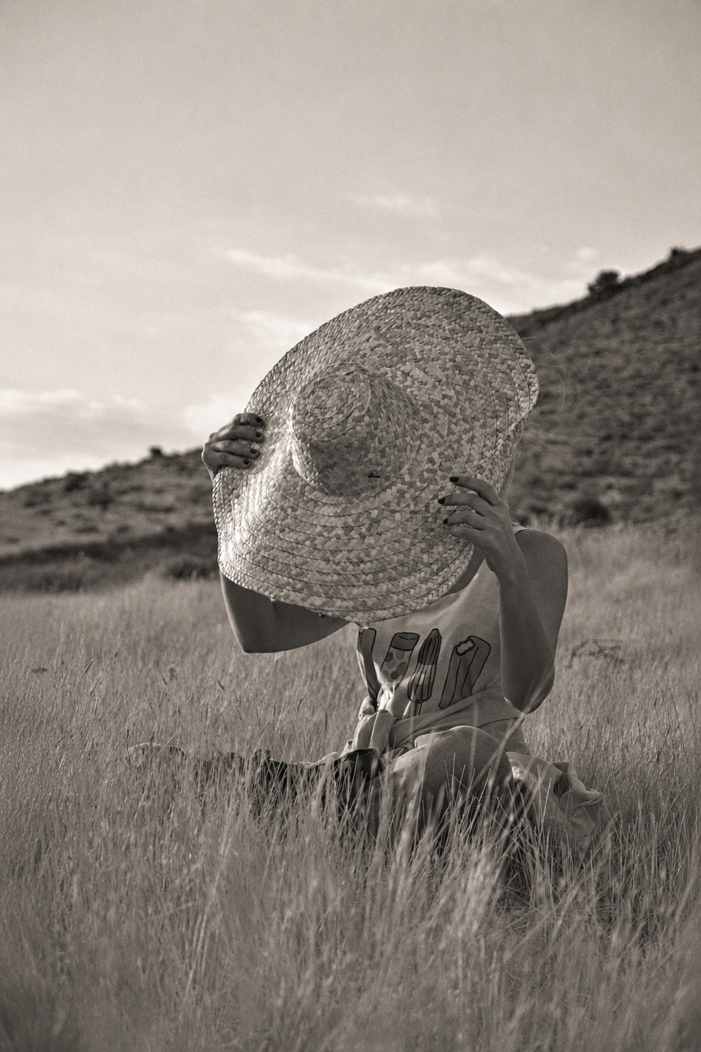 A summer hat on a faceless wooden bust seen in profile, in soft warm black and white.