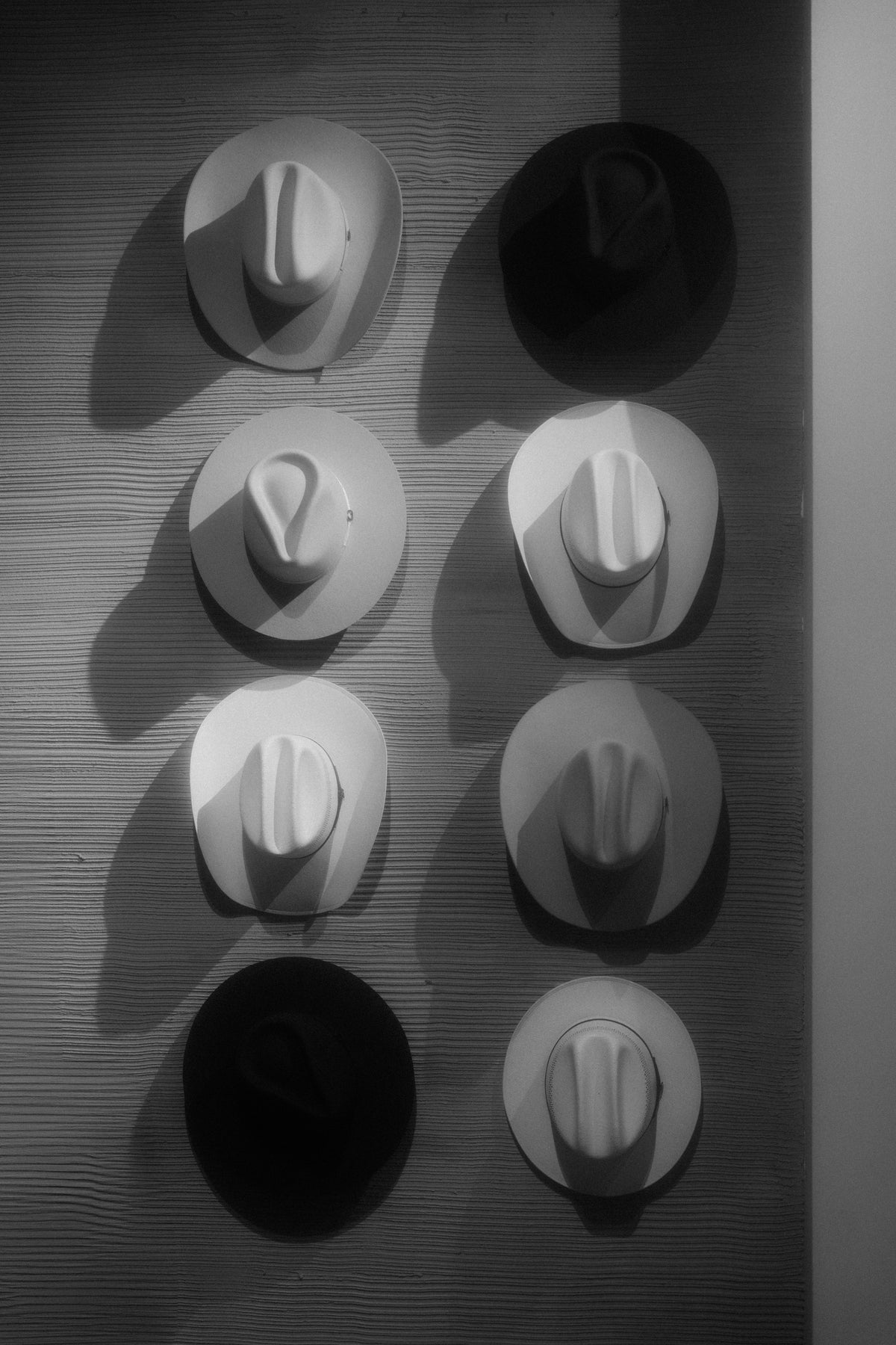 A wide-brim cowboy hat resting on a wooden hat stand against a plain, pale background.