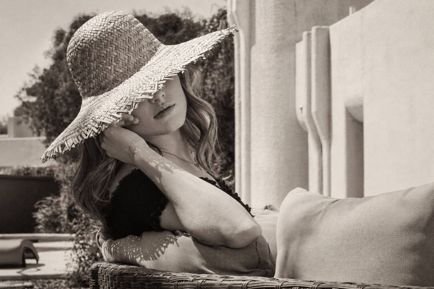 A summer hat resting on a faceless wooden form, its wide soft brim in view, in warm black and white.