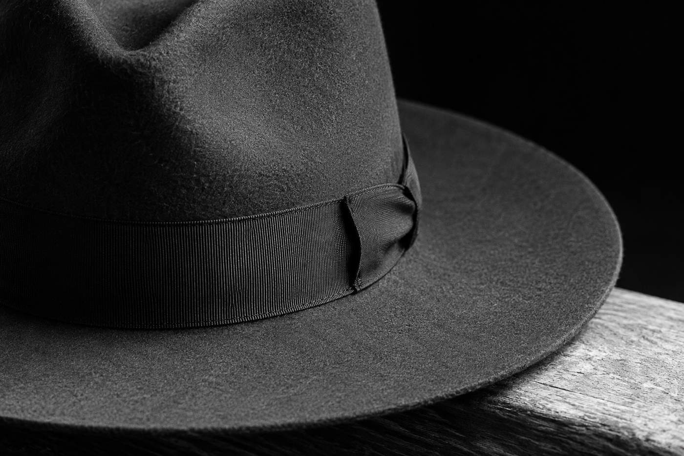 Close black-and-white detail of a wide-brim fedora, showing the grosgrain ribbon band where it meets the crown and the clean brim edge.
