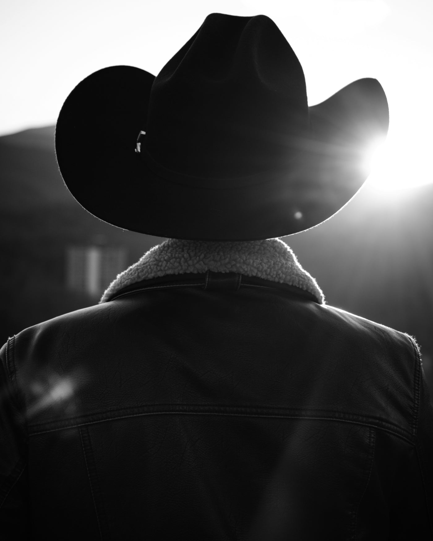 A person seen from behind in a wide-brim cowboy hat, lit softly from behind, in black and white.