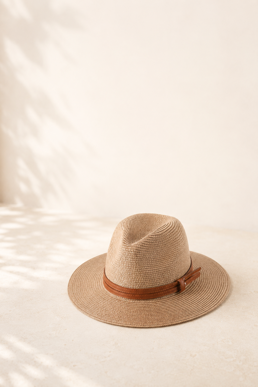 A wide-brim hat with a slim tan band resting on a cream surface in soft daylight.