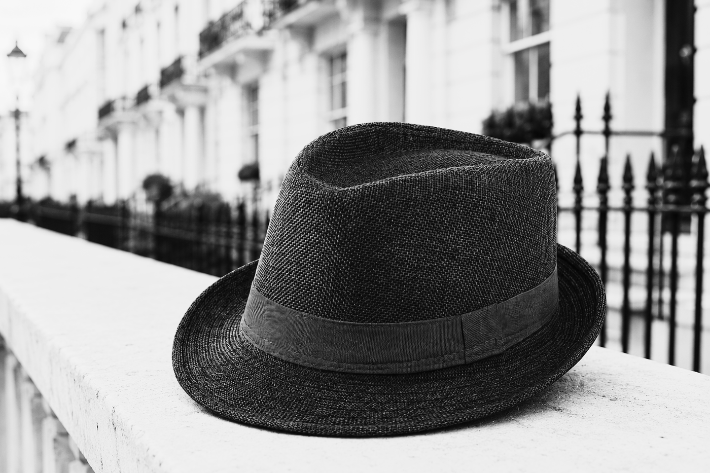 A trilby hat on pale wood, its short brim and pinched crown in view, photographed in black and white.