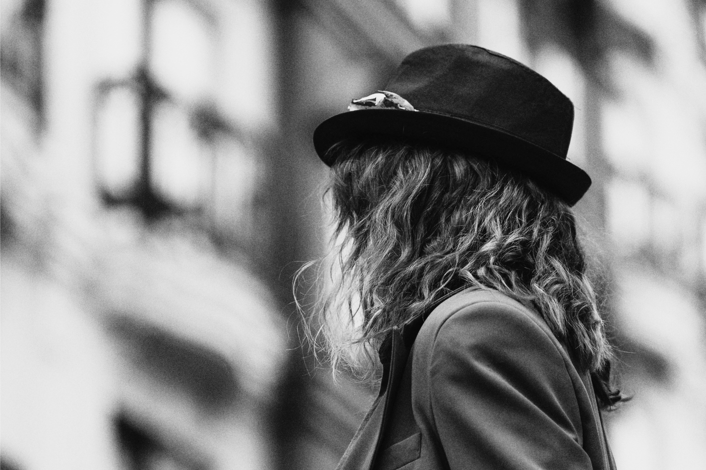A woman seen from behind, wearing a trilby with knitwear, photographed in soft black and white.